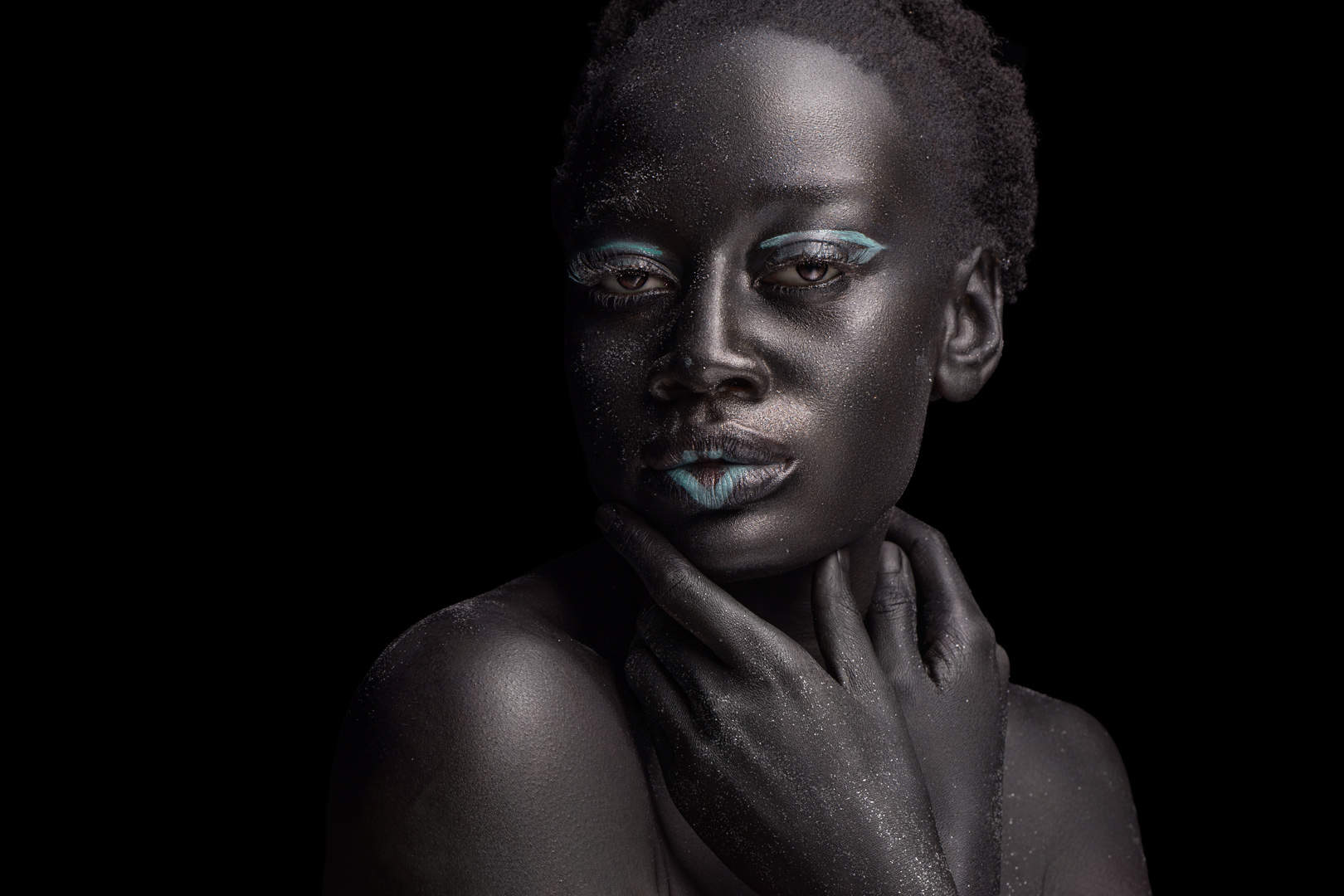 Front-facing beauty portrait with glitter skin, teal eyeliner, and teal lip accent against black