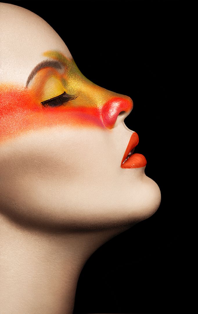Extreme close-up profile with bold orange and gold fire-inspired makeup against black background