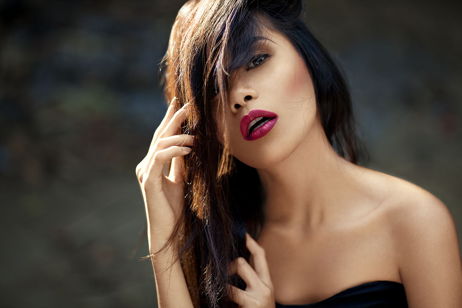 Outdoor beauty close-up with berry lips, hair partially covering one eye, and soft bokeh background