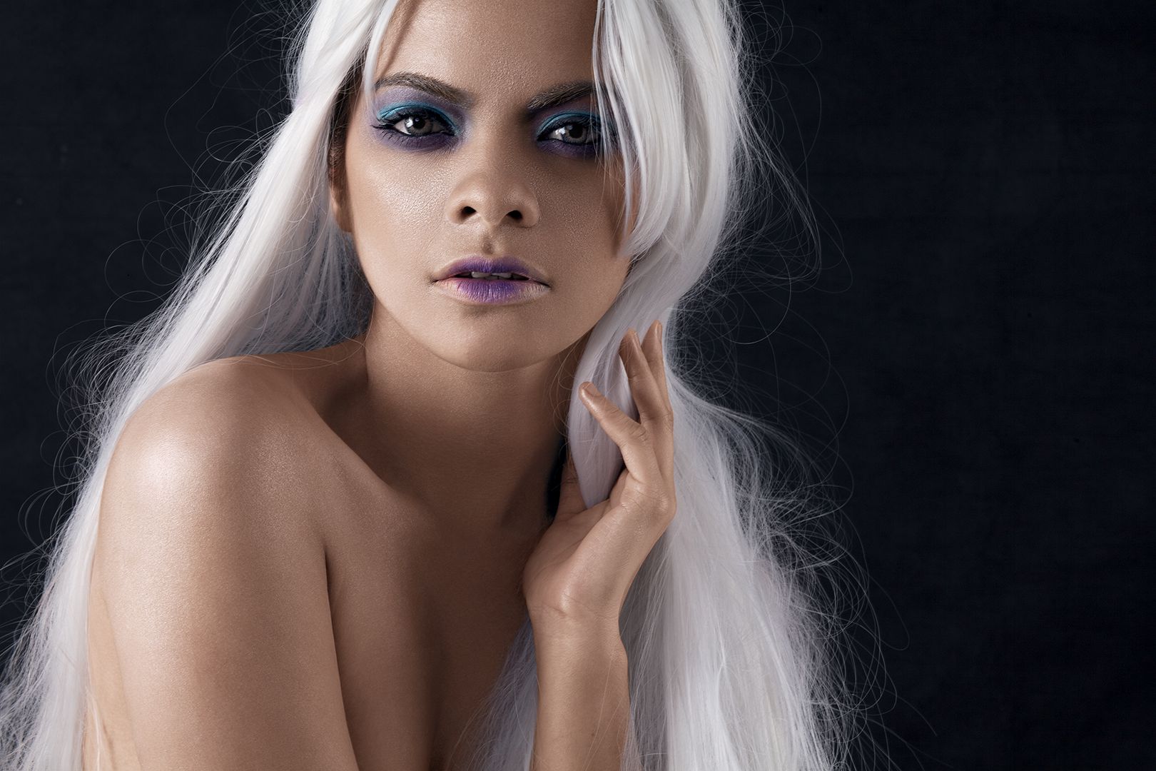 Beauty portrait with platinum white hair, purple-blue eyeshadow, and lavender lips against dark background