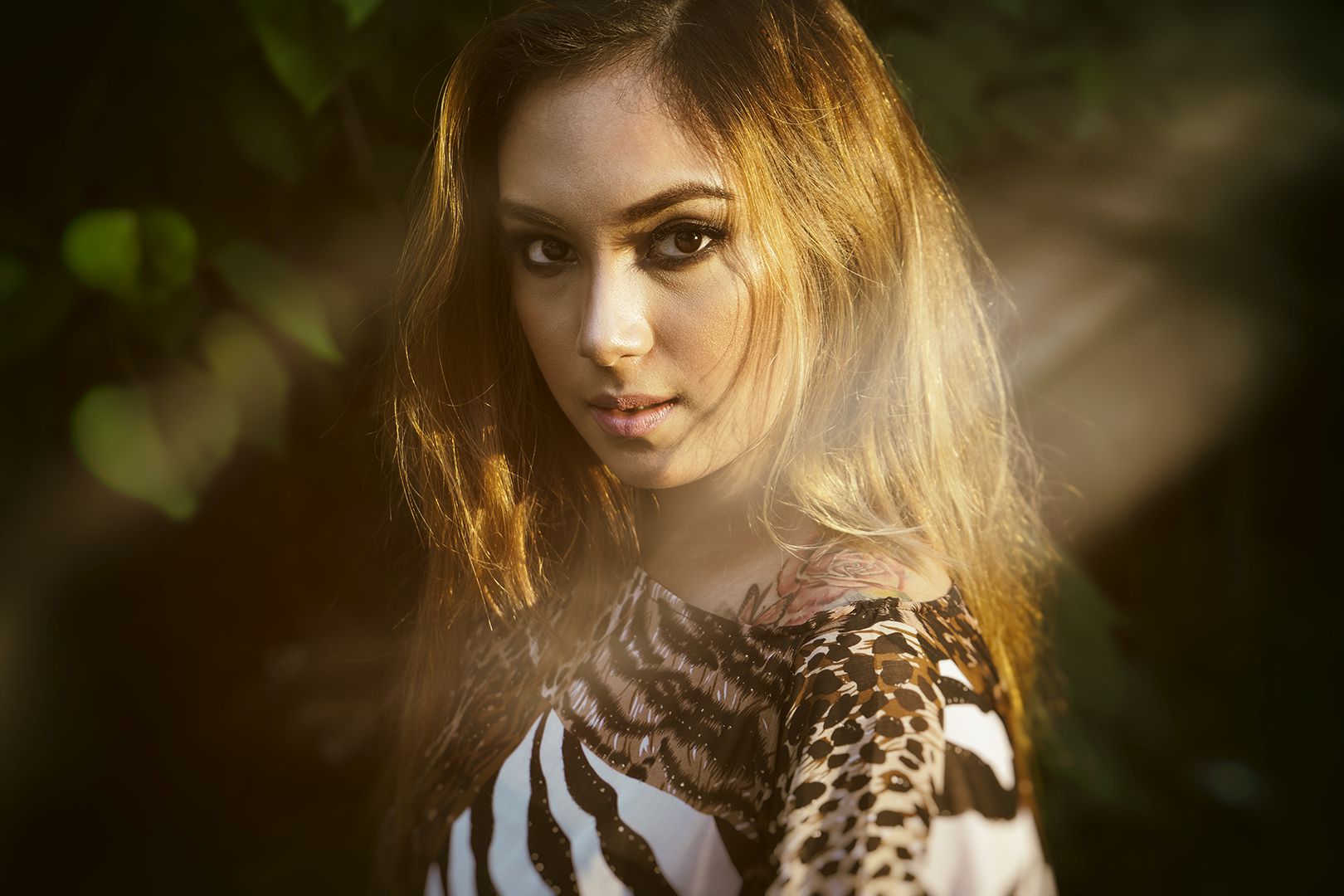 Editorial portrait in golden hour sunlight with animal print top, tattoos visible, direct gaze through hair